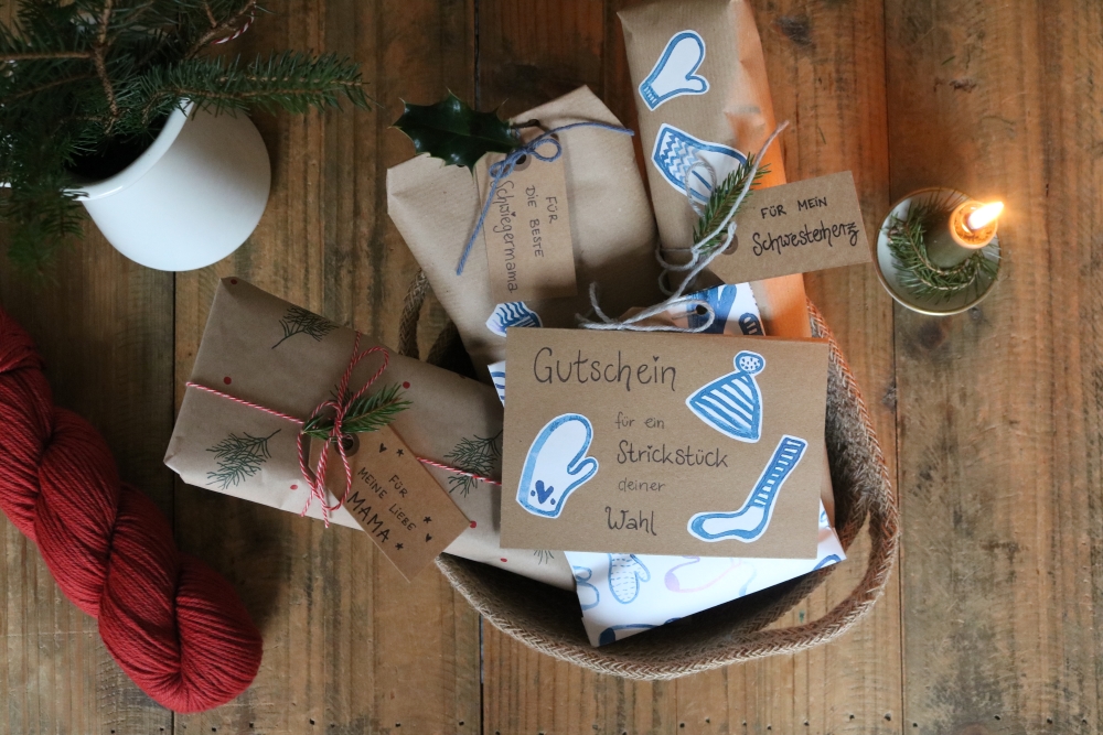 Presents wrapped in brown paper and lovingly decorated on a background of dark wood, next to them a skein of yarn in dark red, a burnung candle and a few fir branches